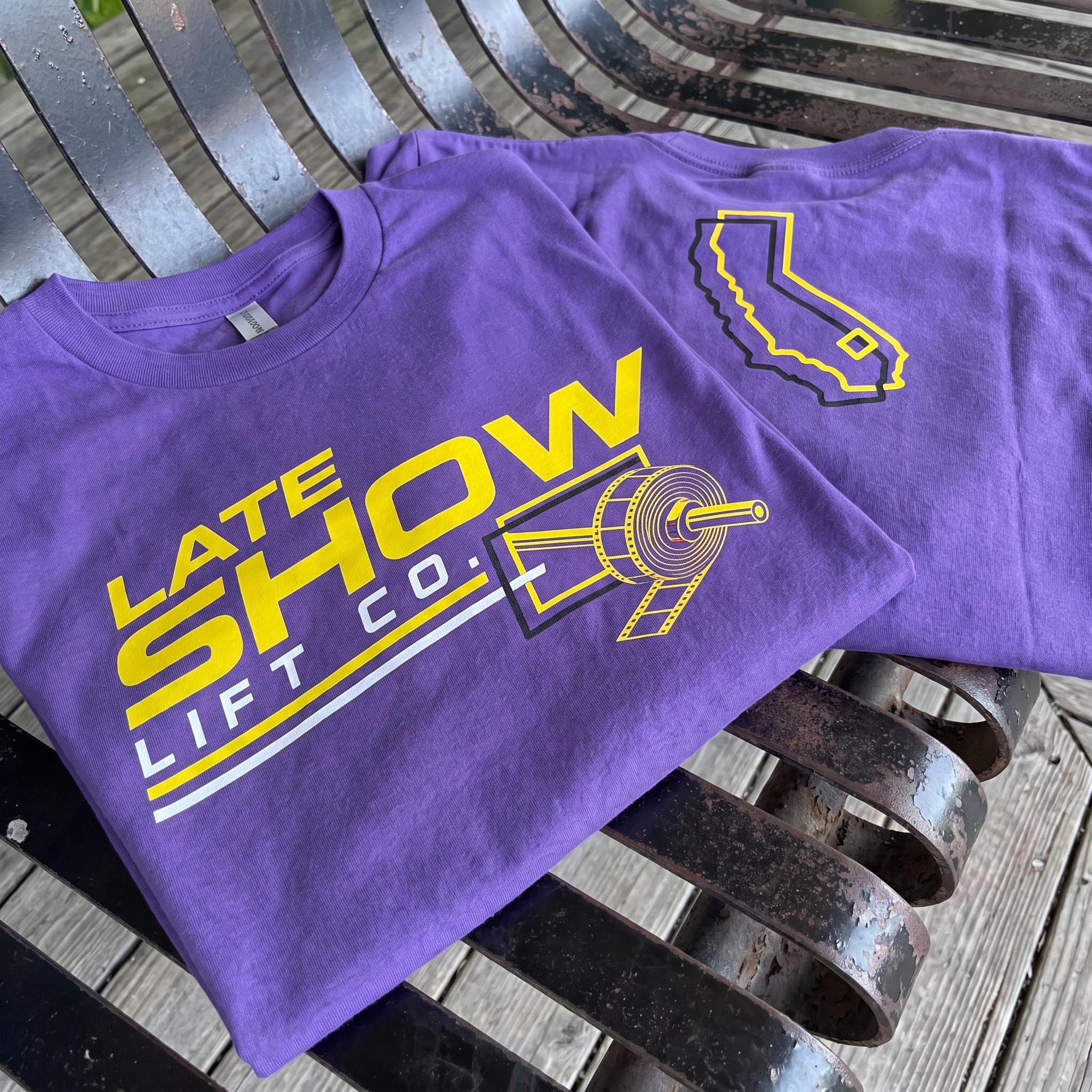 Late Show Lift Co purple and gold tees with barbell film reel graphic
