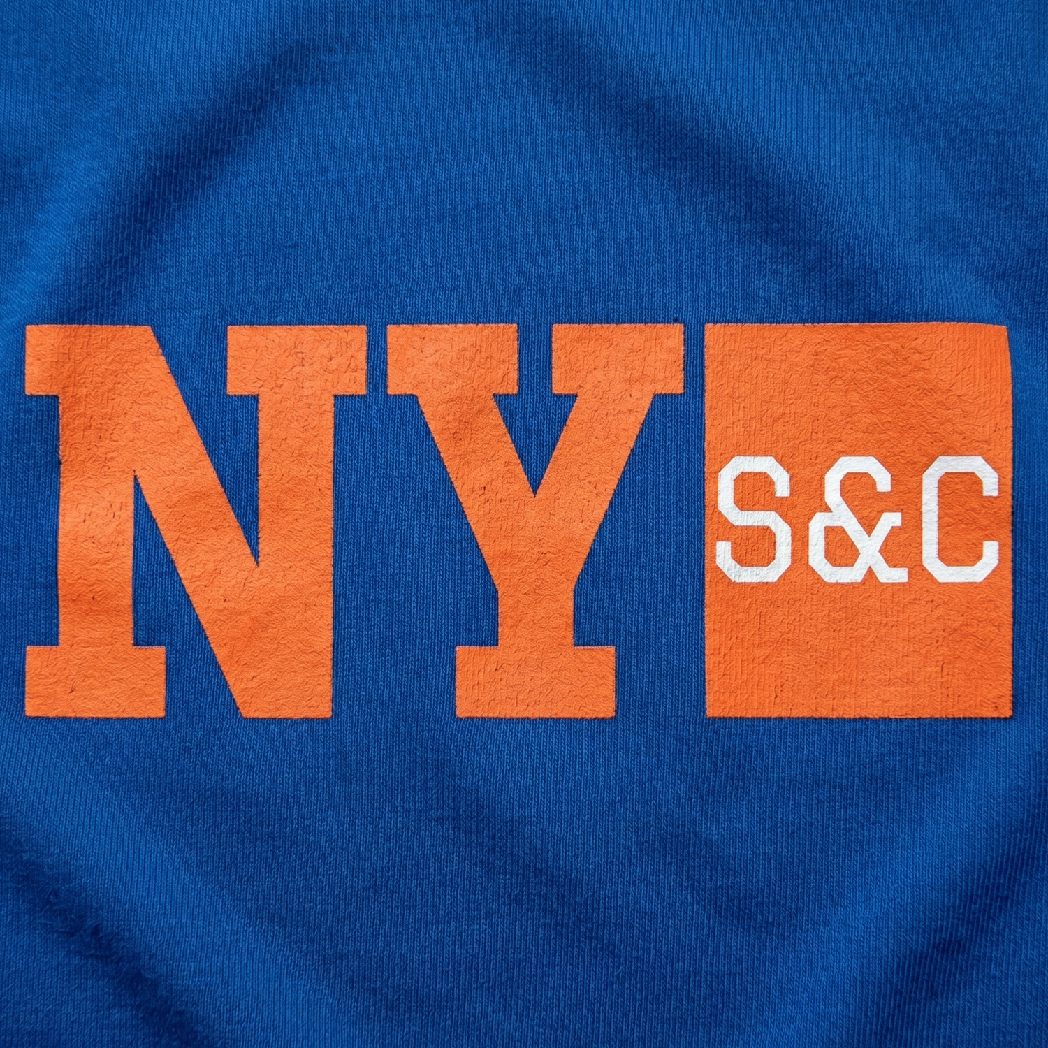Close-up of New York Strength and Conditioning screen printed NY S&C logo in orange and white on blue fabric