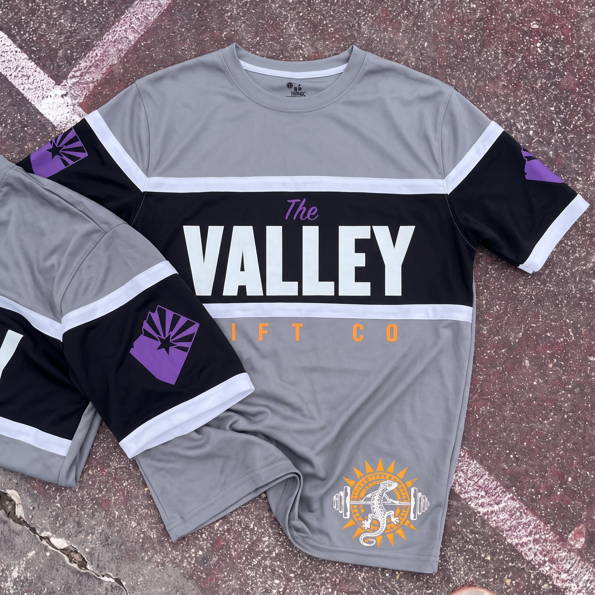 The Valley Lift Co full apparel lay flat with orange tee, grey joggers, purple tee, grey performance jersey, black tee, orange hoodie, and rope cap