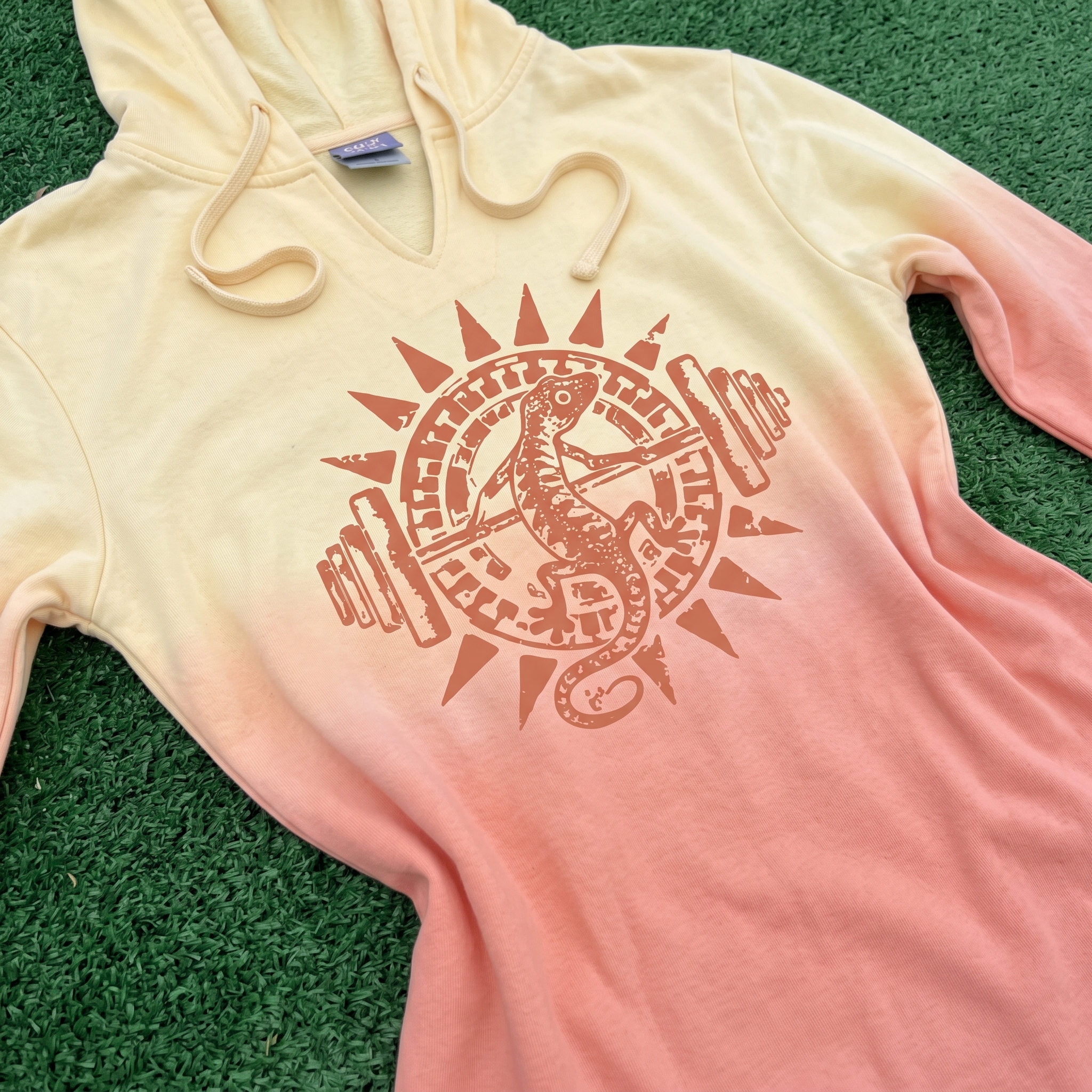 The Valley Lift Co sleeveless hoodie in a cream to peach fade with desert lizard and barbell sunburst graphic