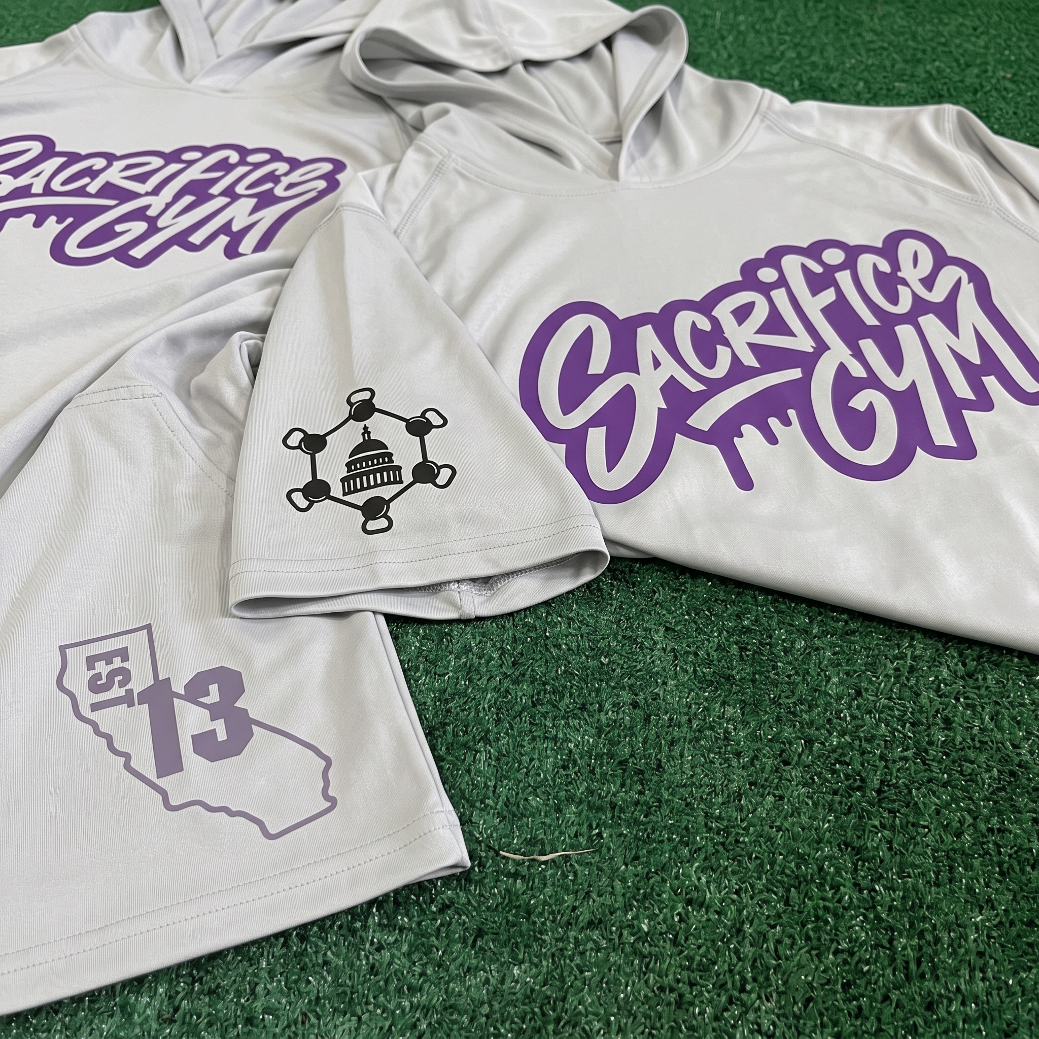 Grey and purple SACrifice Gym raglan shirt laid flat on wooden bleachers