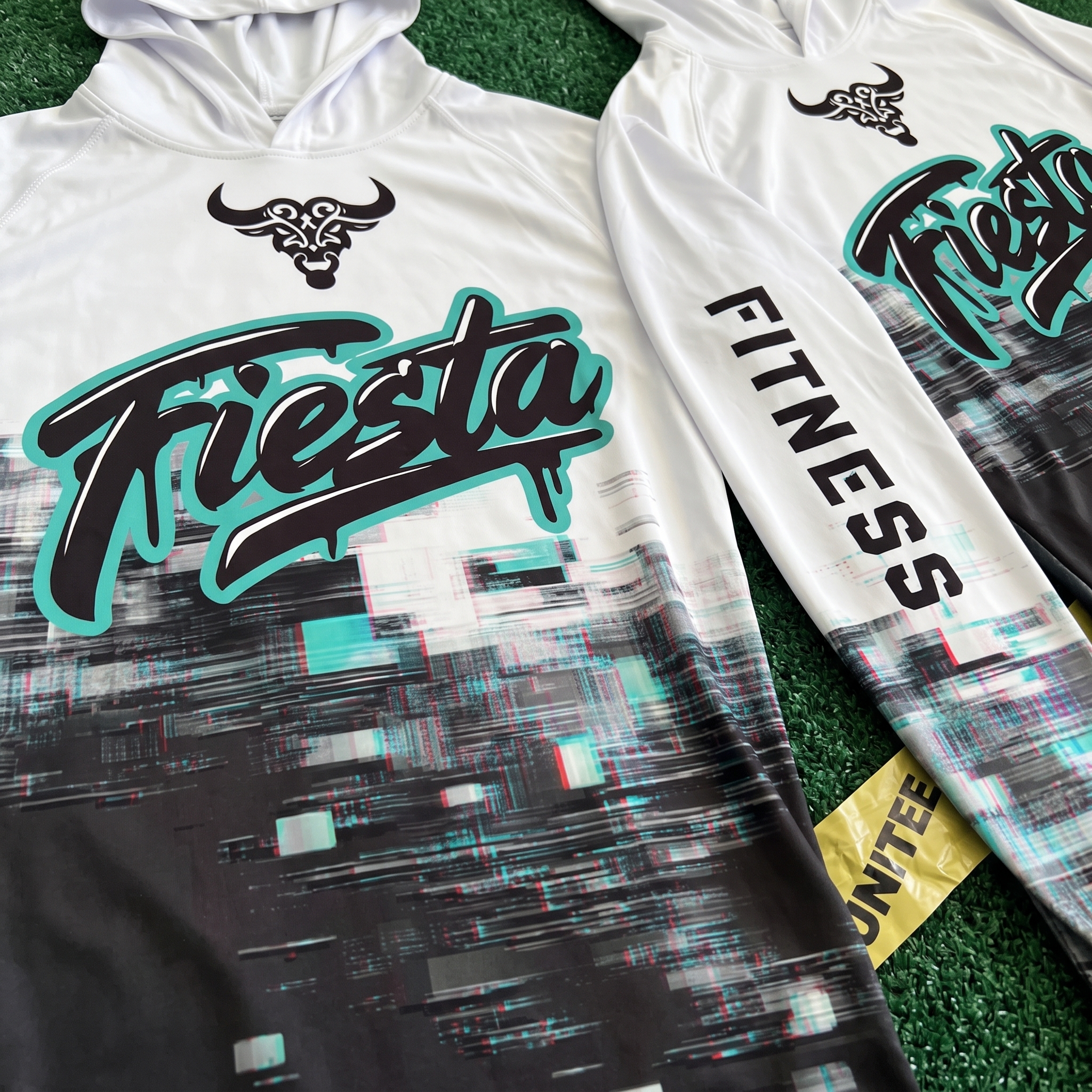 White Fiesta Fitness performance hoodies with turquoise script, bull chest mark, sleeve fitness type, and black glitch texture