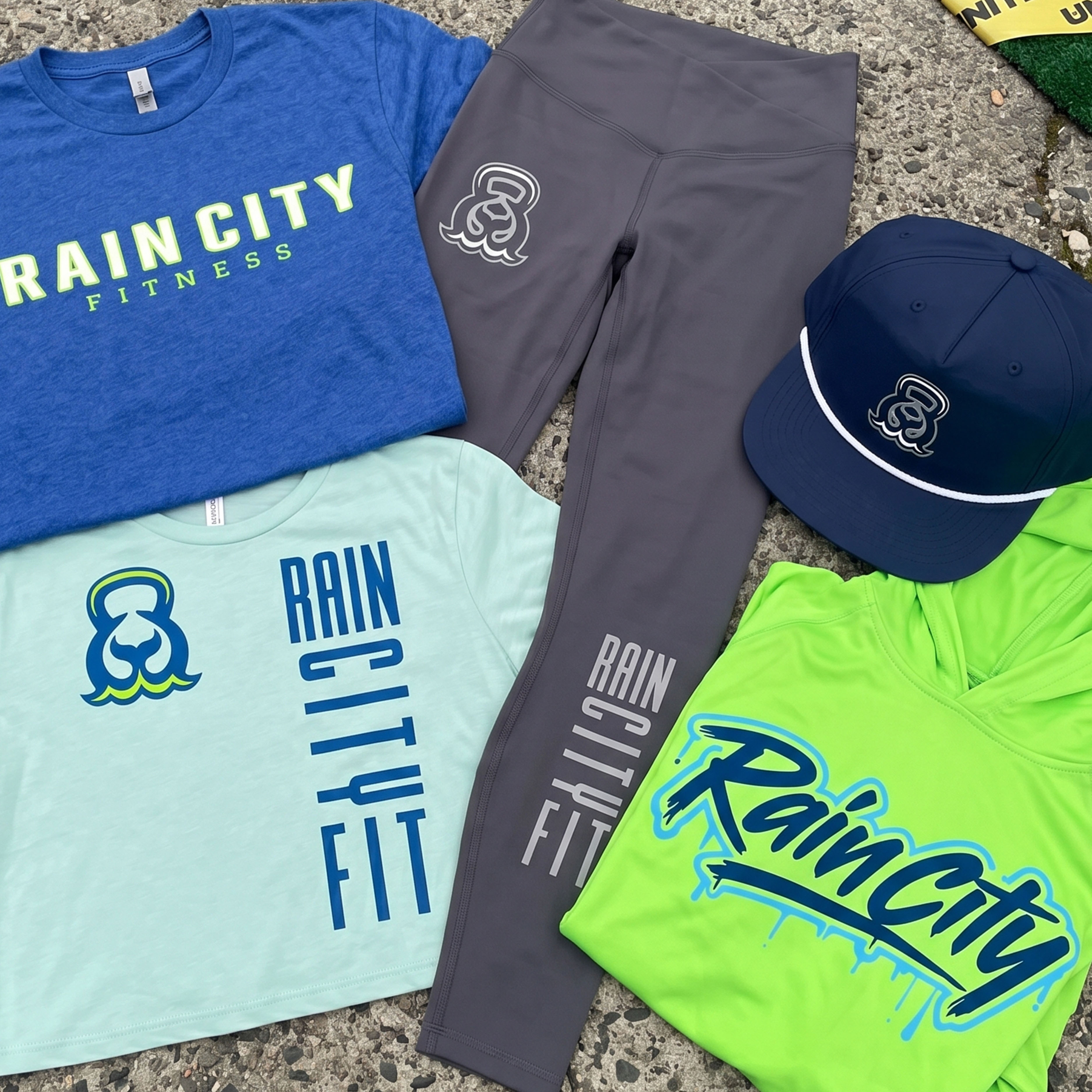 Full Rain City Fitness Seattle apparel collection with blue tee, mint crop tee, grey leggings, navy hat, and neon green hoodie