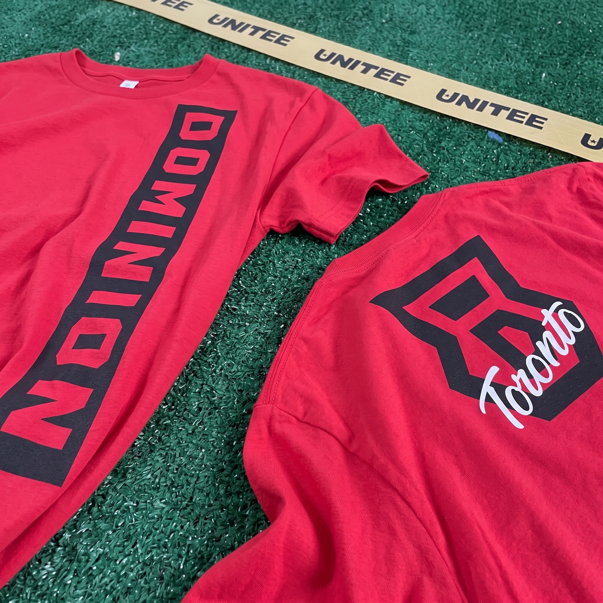 Red Dominion Toronto tee with vertical black Dominion print and shield monogram on back