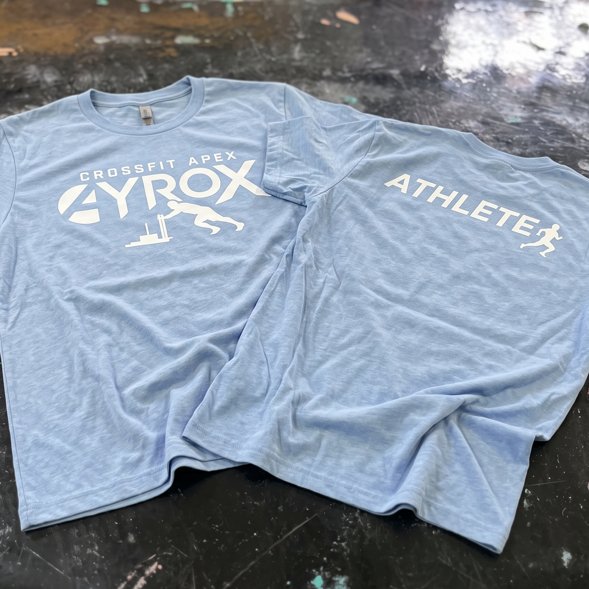 Two powder-blue CrossFit Apex HYROX tees with white front and back athlete graphics.