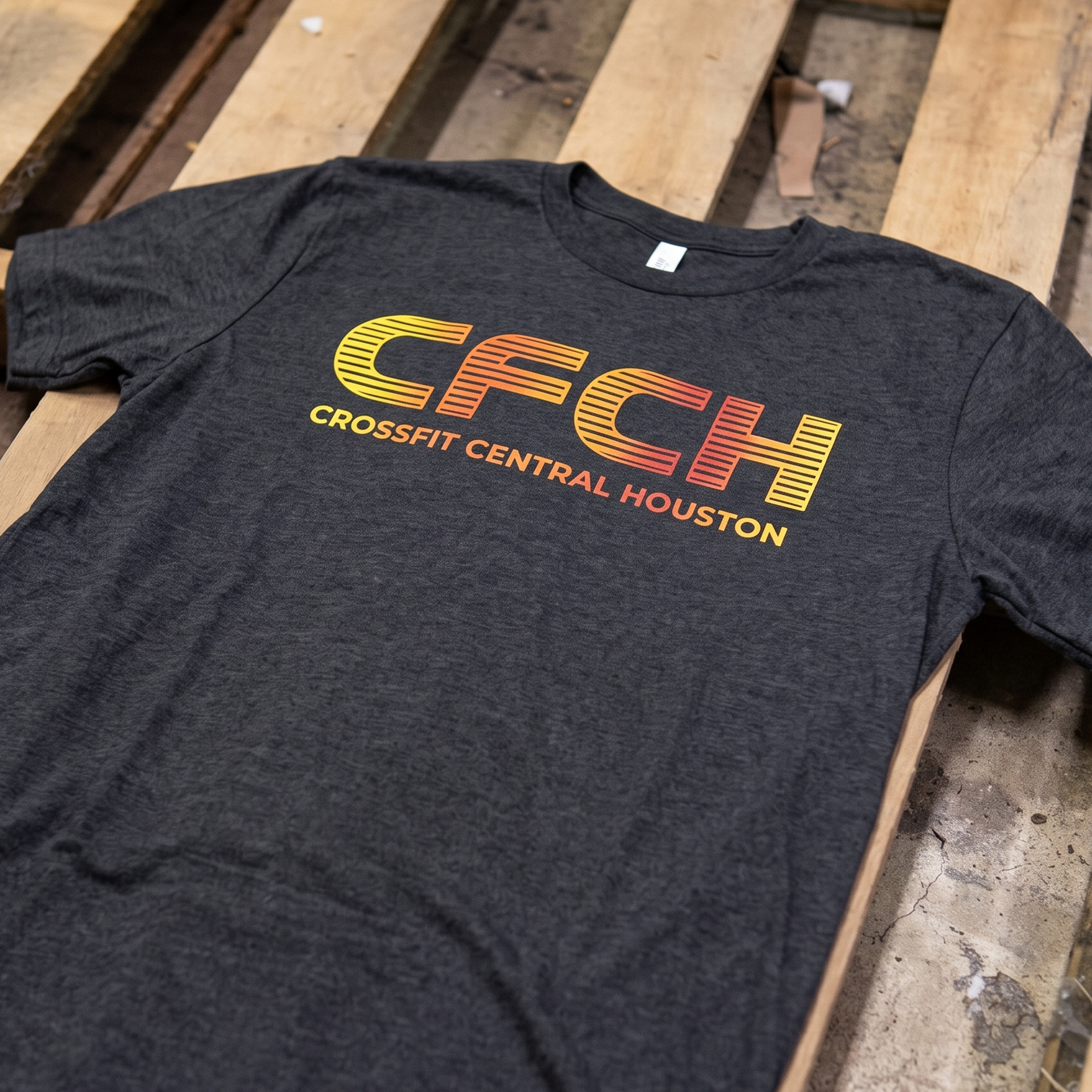 Charcoal tee with striped CACH lettering in a yellow-to-orange gradient.