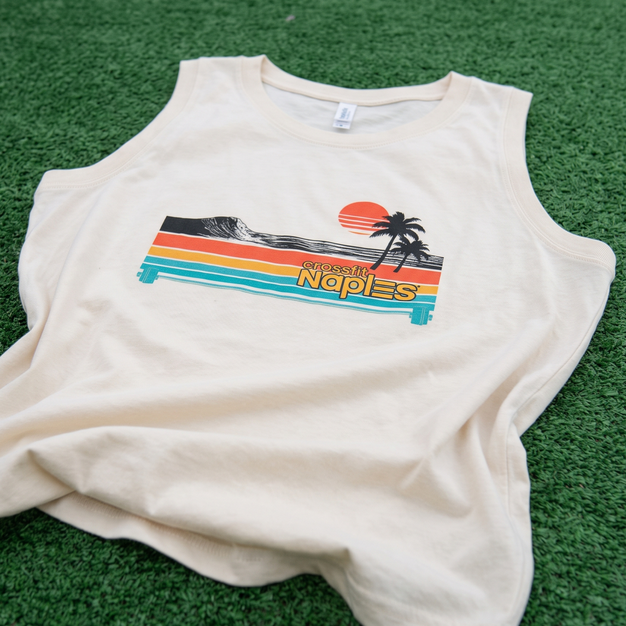Cream CrossFit Naples tank with striped sunset, wave, palm tree, and barbell artwork.