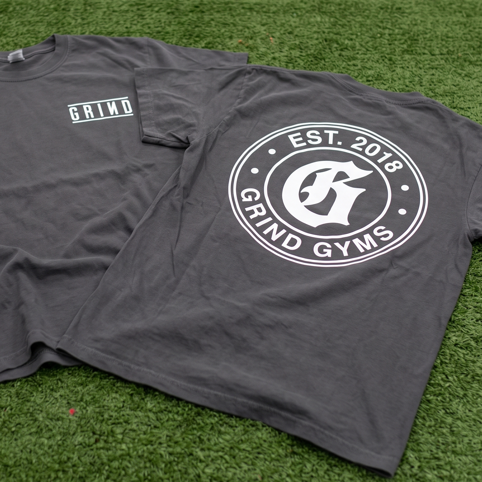 Charcoal GRIND tees with a small chest wordmark and large circular back emblem.