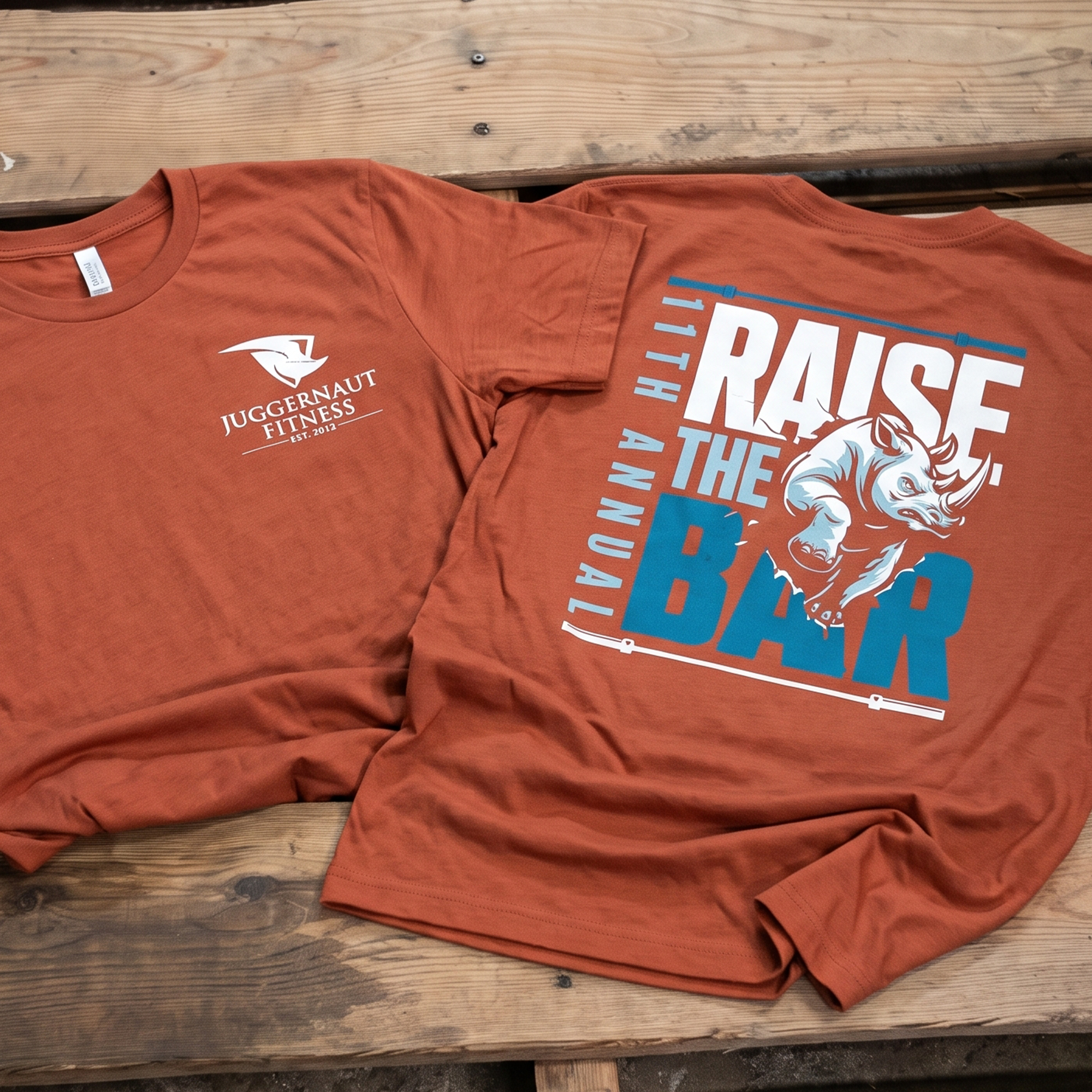 Rust Juggernaut Fitness tee with a small chest logo and Raise the Bar rhino back graphic.