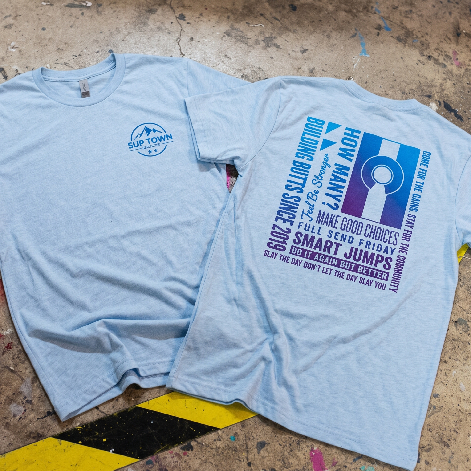Light blue Sup Town CrossFit tee with a small mountain chest logo and blue-purple typographic back print.