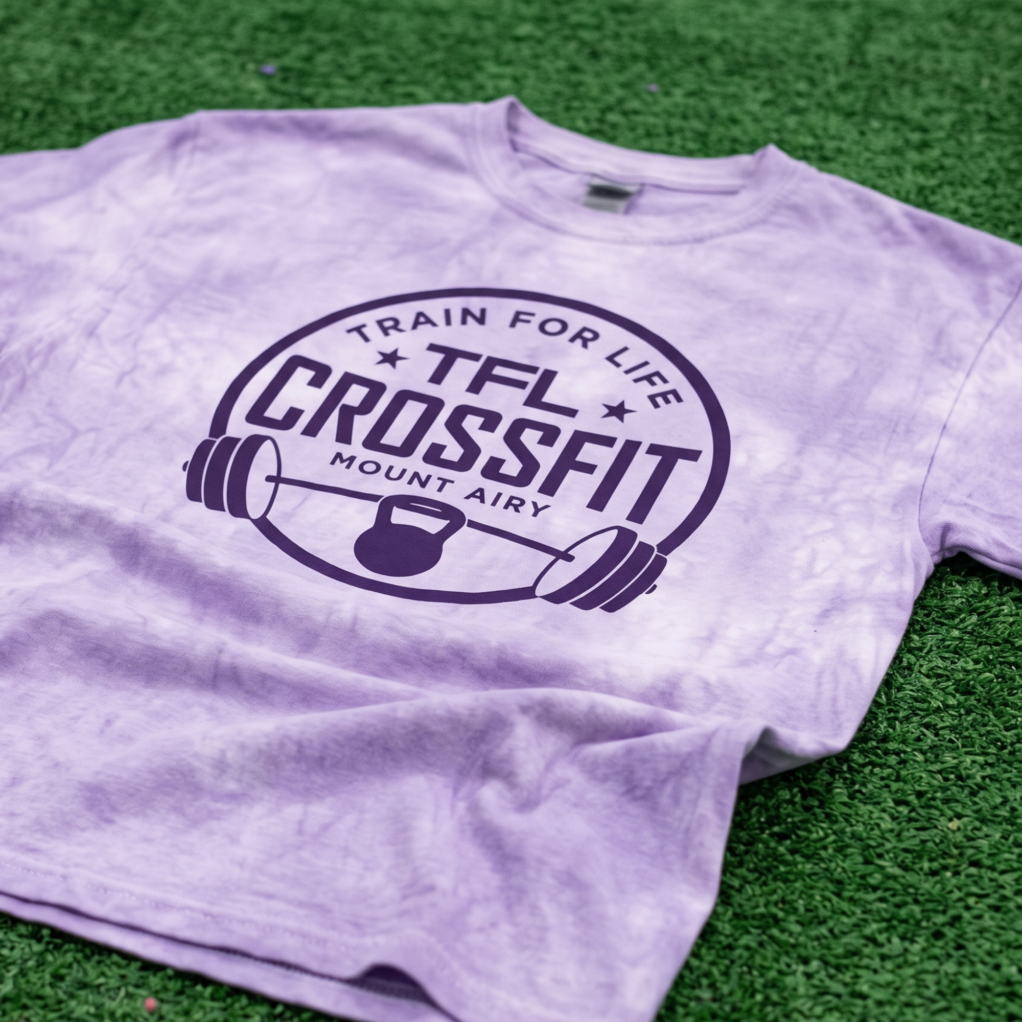 Lavender tie-dye TFL CrossFit tee with purple badge graphic, barbell and kettlebell illustration.