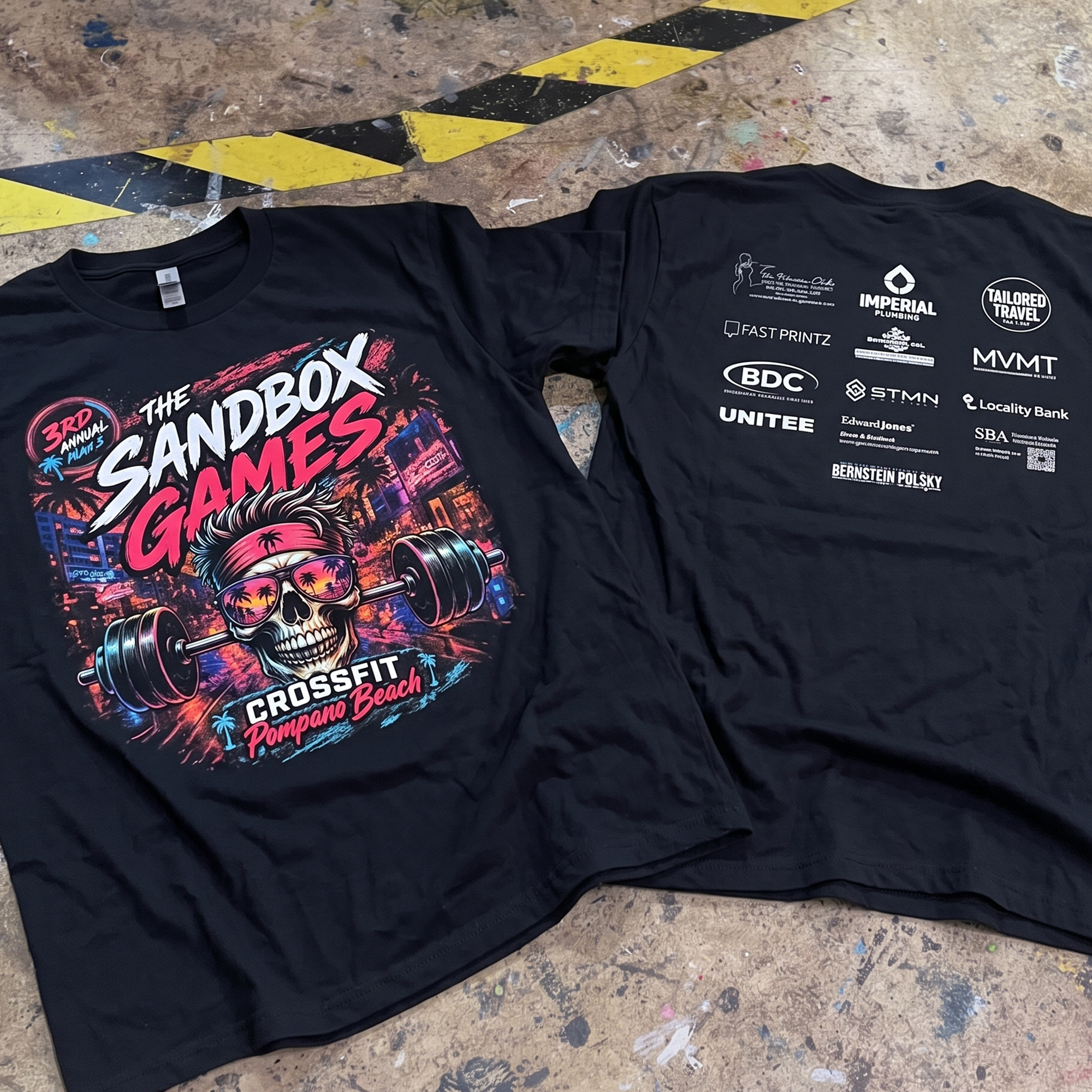 Black tee with neon skull, barbell and Sandbox Games graphic on front, plus white sponsor logos on back.
