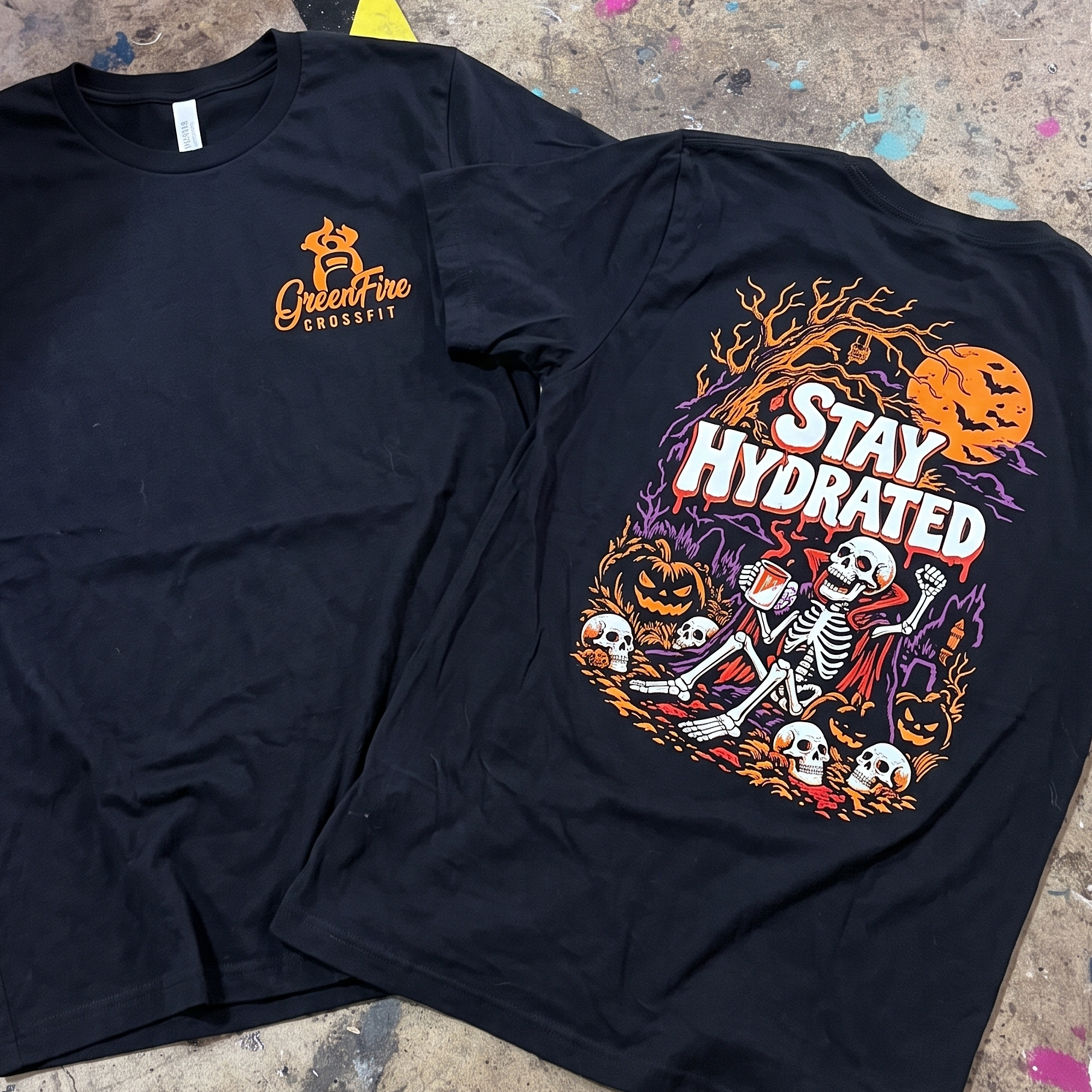 Black T-shirt with orange chest logo beside Stay Hydrated skeleton back print.