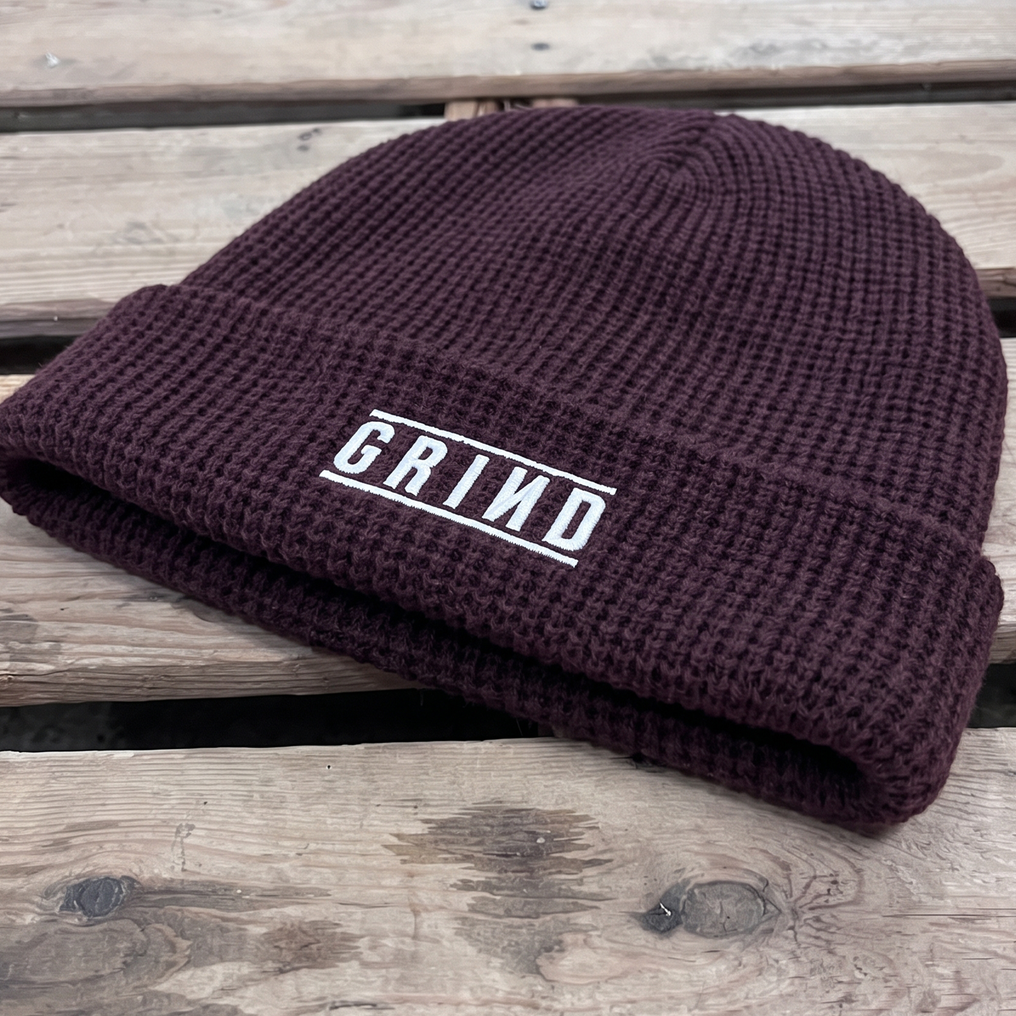 Deep burgundy rib-knit beanie with a white framed GRIND wordmark