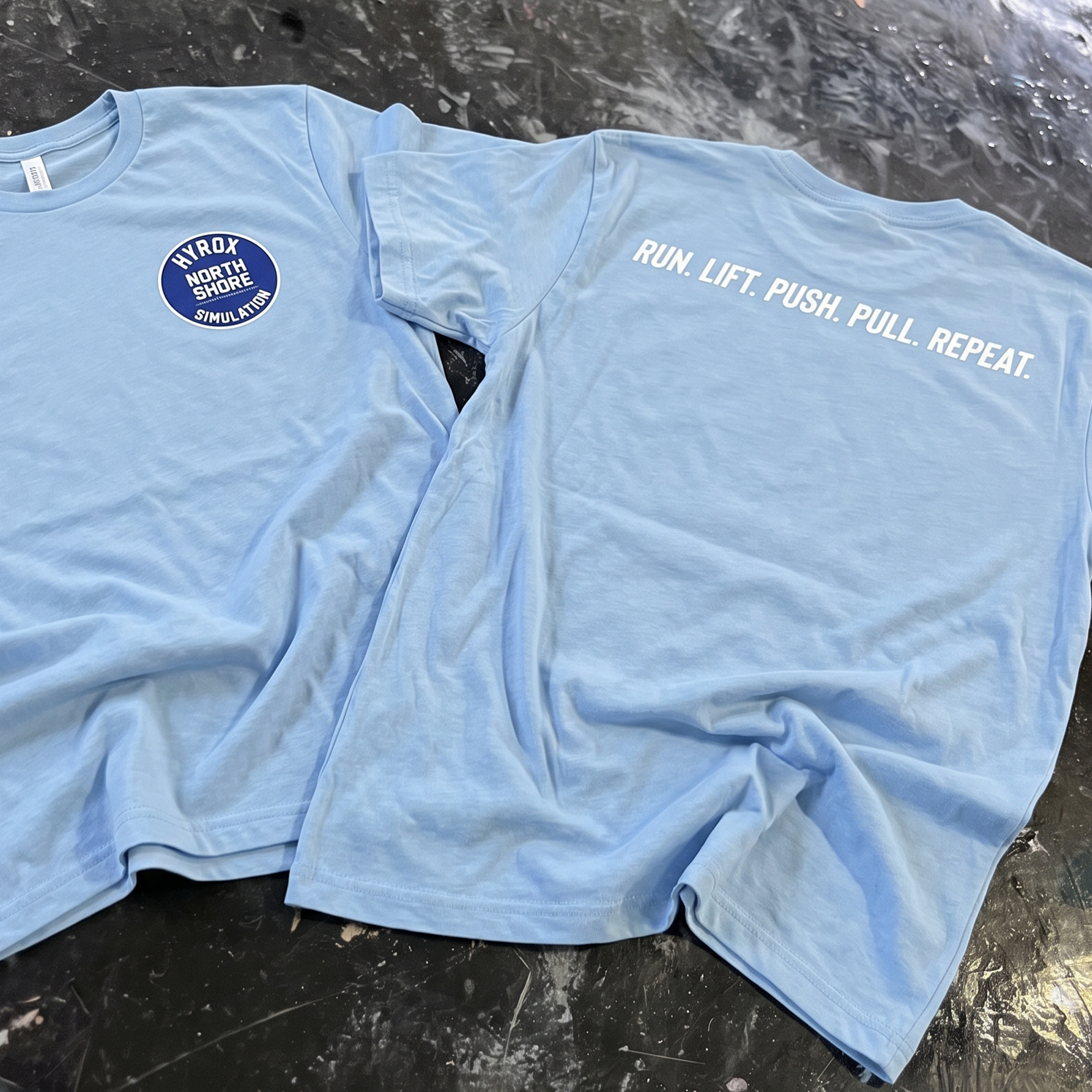 Powder-blue tee with a navy HYROX simulation chest badge and back slogan.